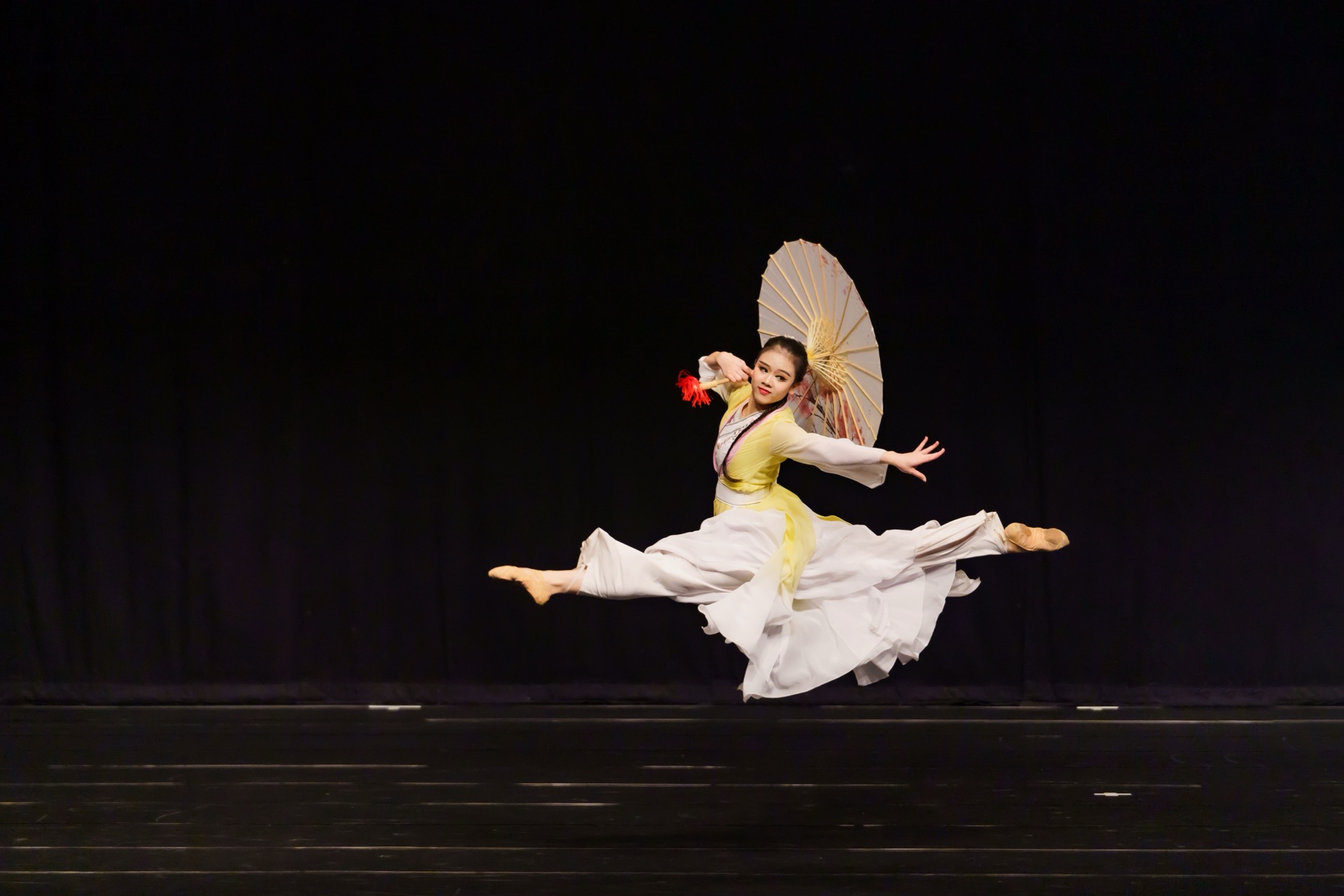 舞蹈攝影服務 — 身著白黃舞衣手持油紙傘的舞者於舞台上騰空躍起