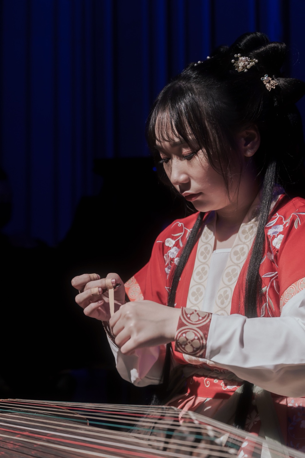 音樂會側拍作品 — 身著紅色漢服的演奏者專注彈奏古箏