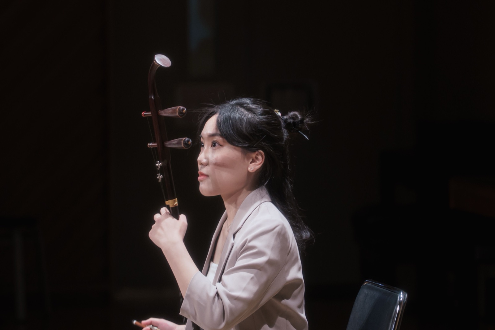 音樂會側拍作品 — 身著淺色套裝手持二胡的演奏者神情專注