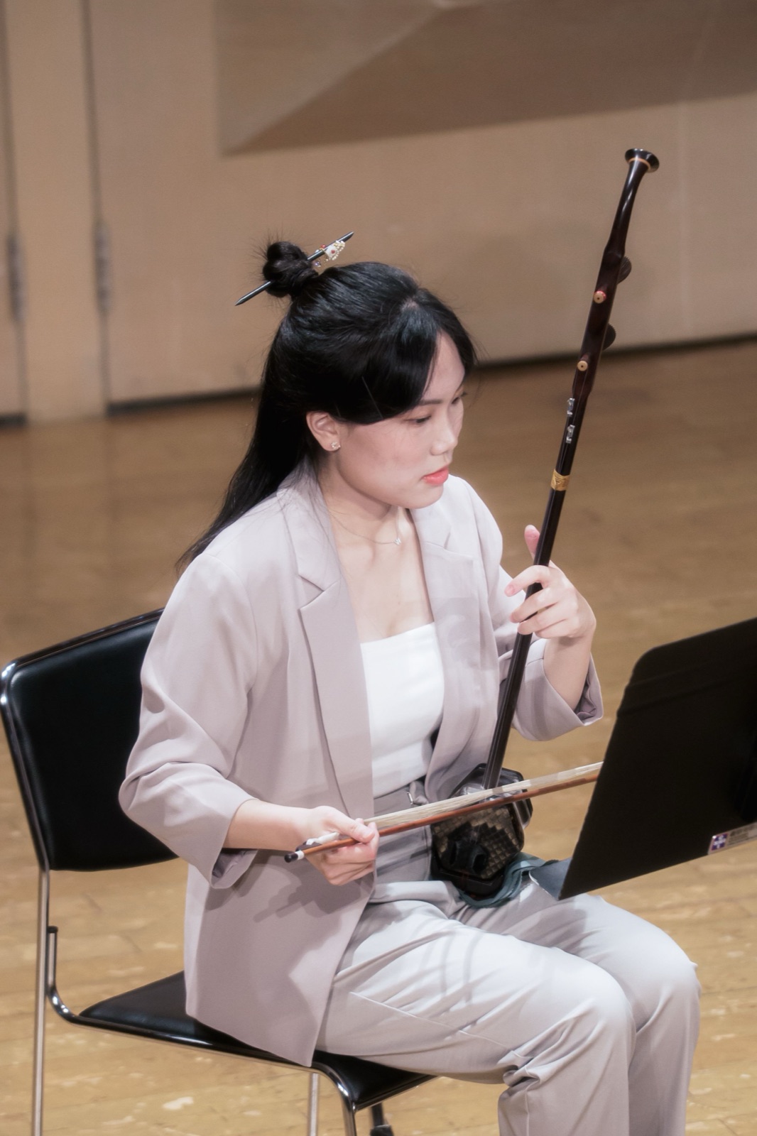 音樂會側拍作品 — 身著米色套裝的二胡演奏者坐姿演奏